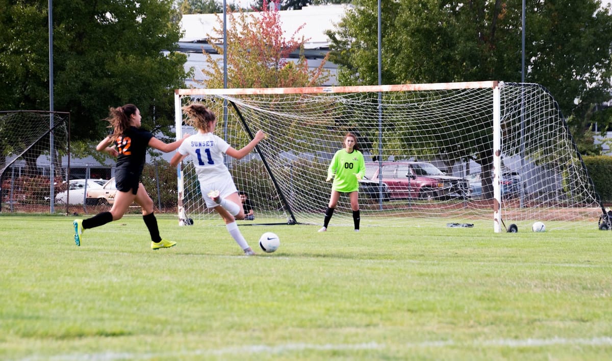 Women athletes competing in a lively soccer game with a goalkeeper defending the goal.